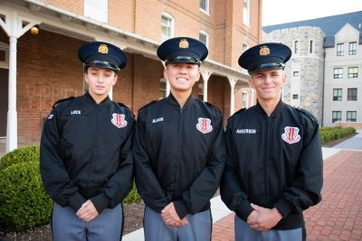 Cadets in uniform stand smiling in front of the historic brick of Lane Hall. 