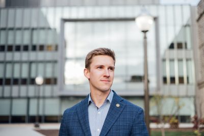 Sam Kennedy, a student veteran in a blue blazer, stands in front of a building on Virginia Tech campus.