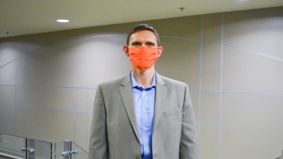 Parks poses with orange mask in suit at the top of a stairwell